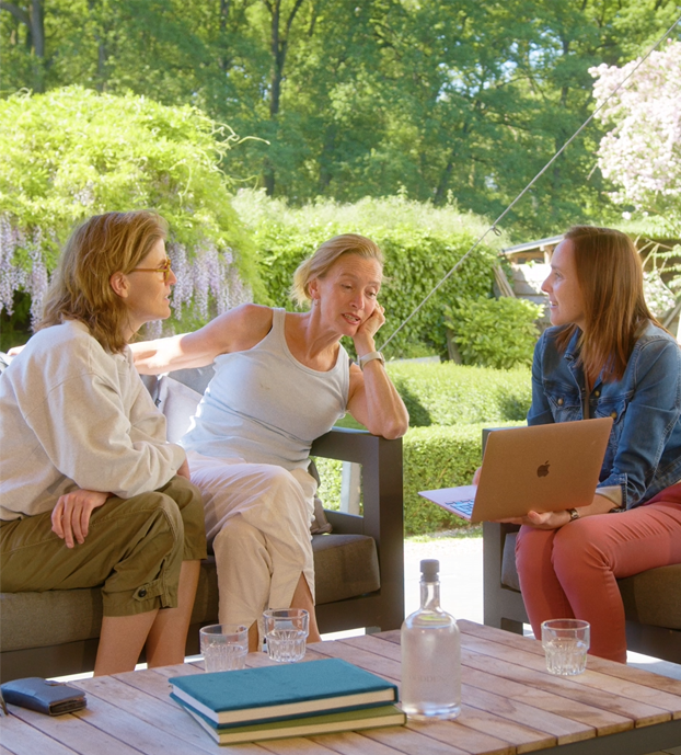 Een eventmanager overlegt lachend met twee gasten aan een tafel op het terras van hun locatie